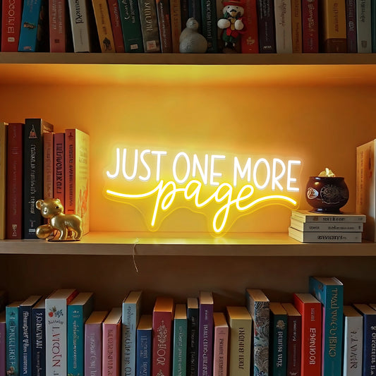 Just One More Page neon sign glowing warm white and yellow on a wooden bookshelf in a cozy home library